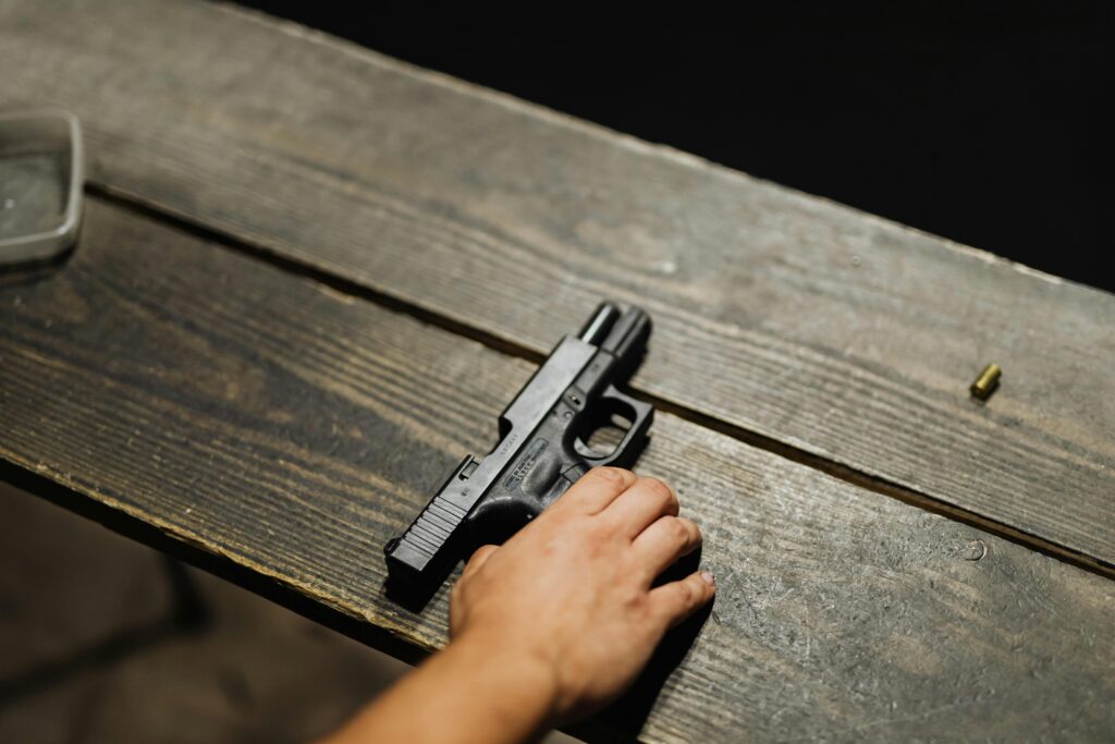 Close-up of a hand holding a handgun on a wooden table with bullet casing.